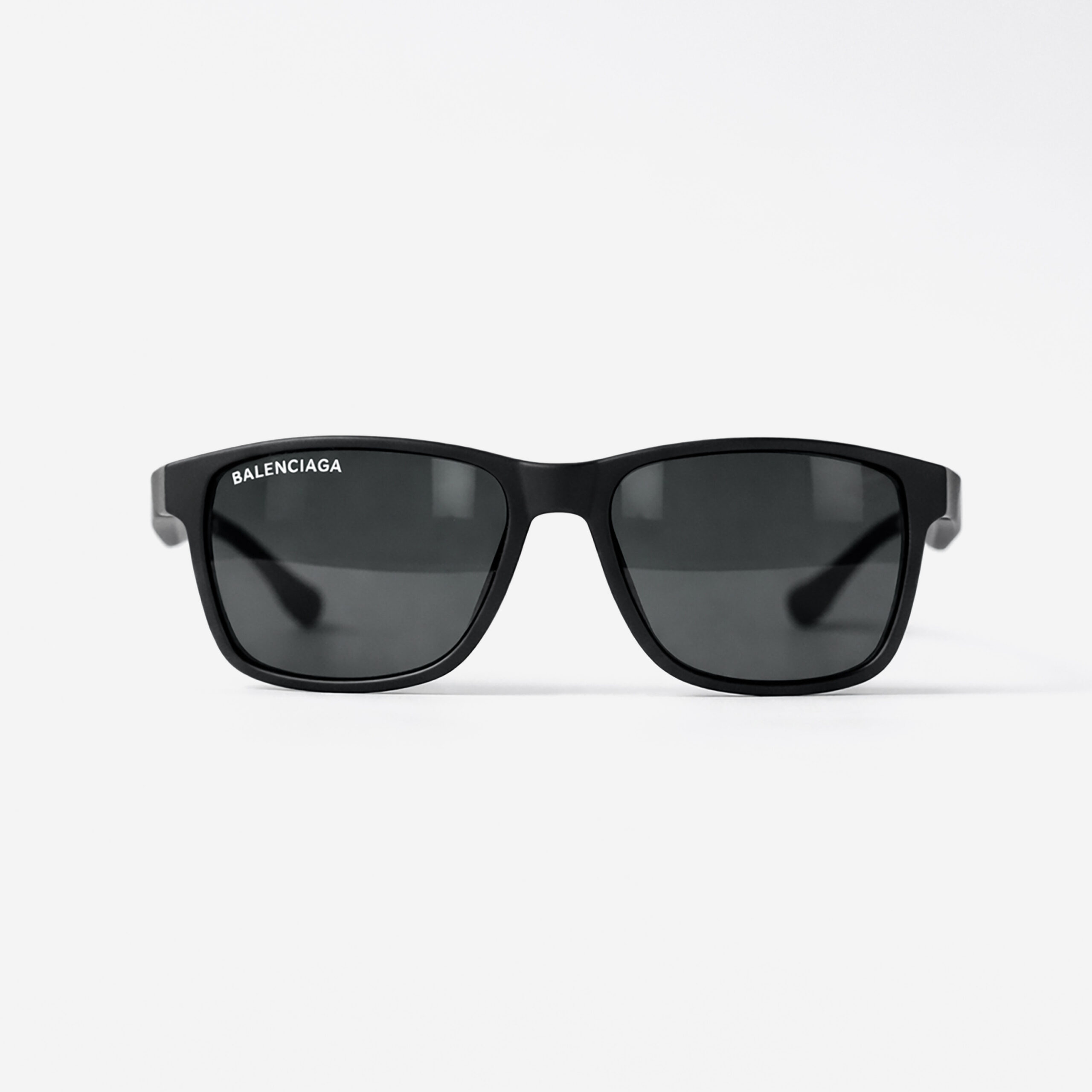 Matte black square sunglasses with dark lenses and a white Balenciaga logo on the lens.